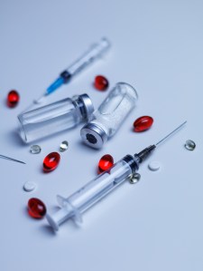 The syringe with the needle taking up the contents of the ampoule. Vaccination concept. Medicine pills or capsules with syringe on white background. Drug prescription for treatment medication. Pharma