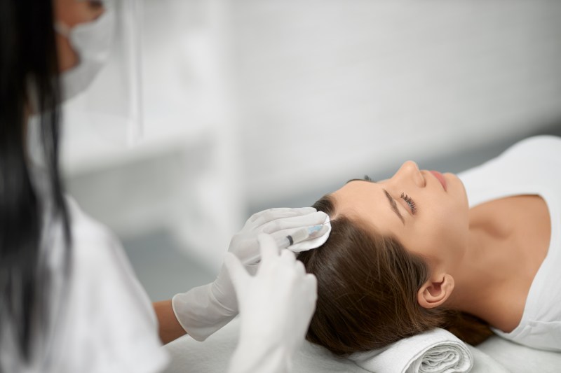 Side view of young cute brunette woman on procedure for improvements hair condition. Concept of different procedure for hair restoration in professional beauty salon.