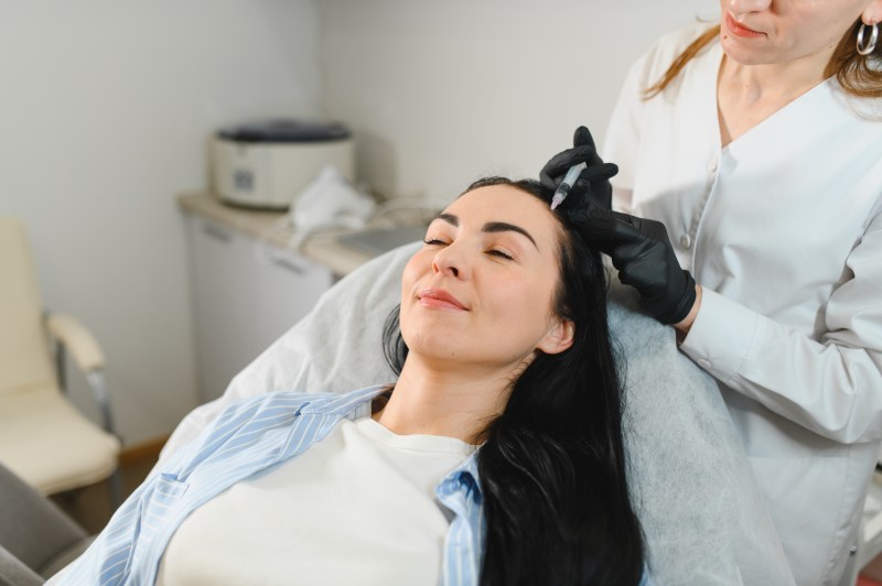 The doctor makes an injection into the head of a girl from hair loss. Hair treatment in a cosmetology clinic.