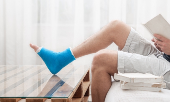 man-with-broken-leg-cast-reads-books-against-light-background-interior-room